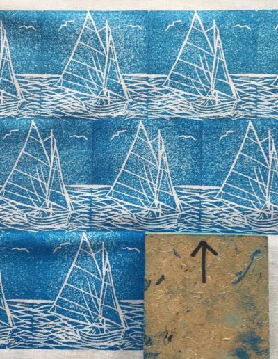 A linocut print of a sailboat printed onto cloth in a repeat pattern