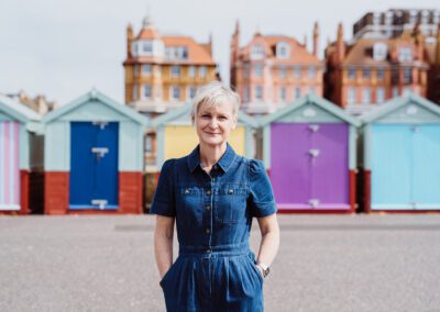 A portrait of Sarah Bagg outside of the colourful beach huts on Hove Seafront